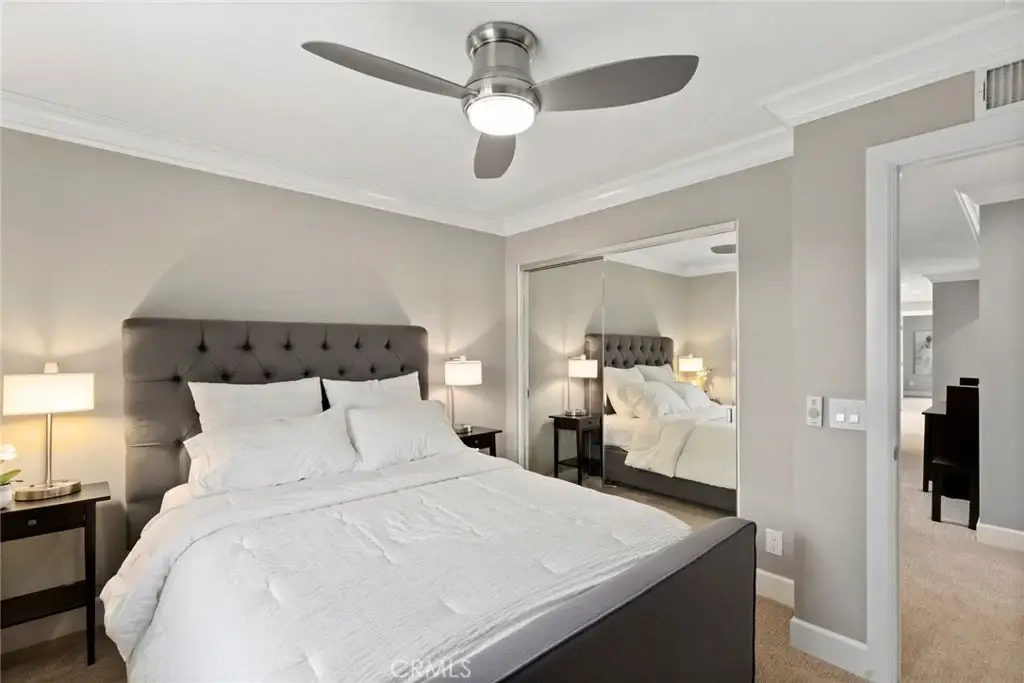 Bedroom with large bed, white bedding, bedside lamps, ceiling fan, and mirrored closet.