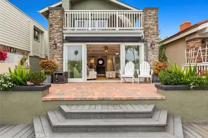 Exterior of house California real estate with stone accents, plants, patio chairs, and steps to glass door.