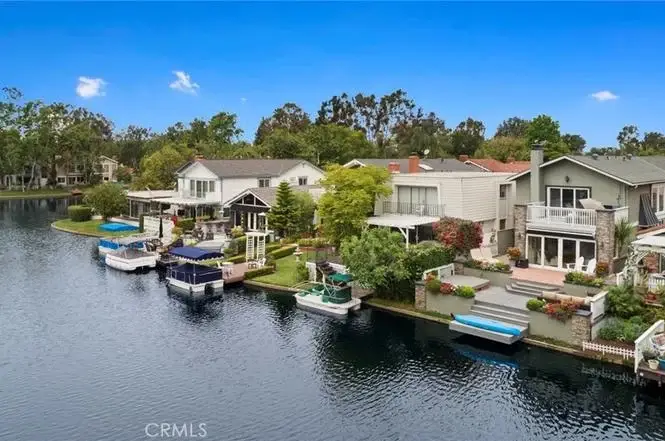Aerial view of waterfront houses California real estate with docks, boats, lake, and green trees.
