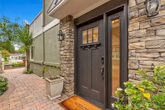 Front entrance of house California real estate with dark wood door, stone wall, welcome mat, plants, and lanterns.