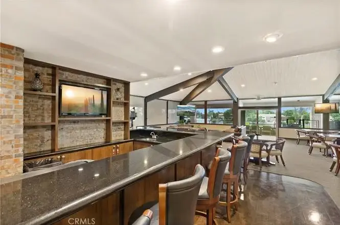 Bar area with counter, stools, wall TV, big window view, and seating in back.