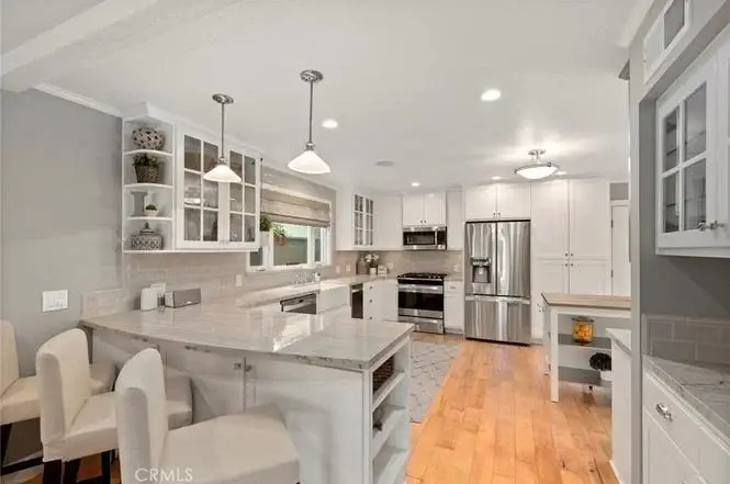 Kitchen with white cabinets, stainless appliances, wood floor, marble island, chairs, and pendant lights.