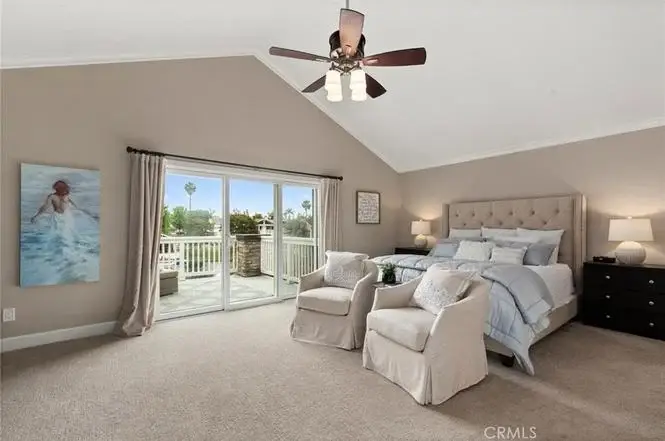 Bedroom with large bed, two armchairs, ceiling fan, wall art, and sliding glass door to balcony.