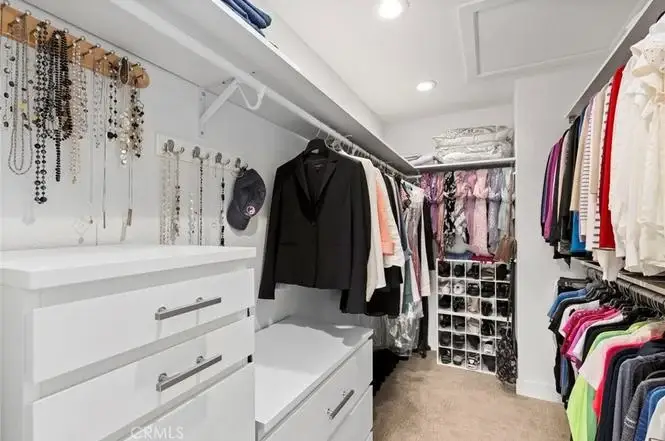 Walk in closet with hanging clothes, shelves with boxes, and jewelry display.