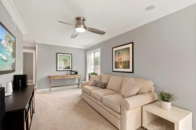 Living room with beige sofa, ceiling fan, wall art, TV, console table, and plants.