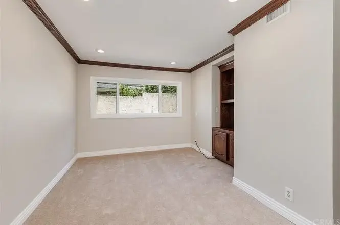 Empty room with light walls, carpet floor, window, and built in shelves.