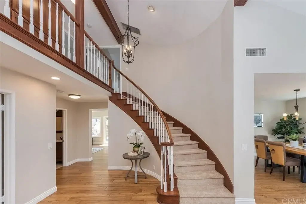 Foyer with curved staircase, wooden railing, chandelier, and hardwood floor