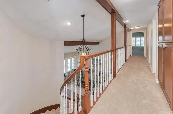 Hallway with wooden railings, beige carpet, chandelier, and doors to rooms