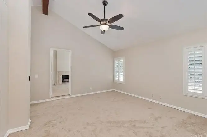 Large room with beige walls, carpet, ceiling fan, and small fireplace