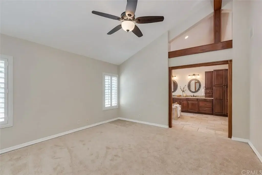 Room with ceiling fan, light walls, carpet, windows, and bathroom doorway