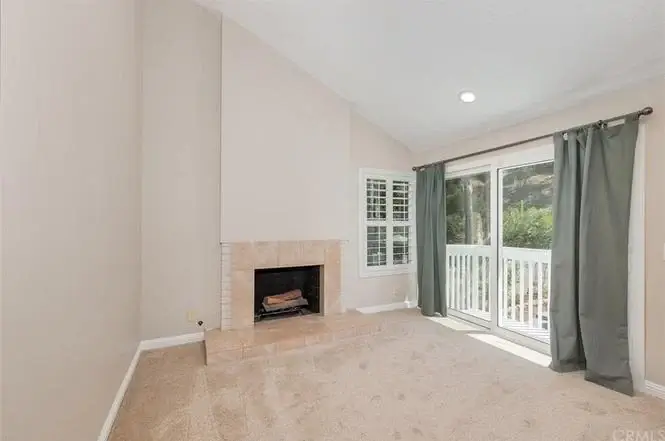Living room with beige walls, stone fireplace, carpet, and balcony doors