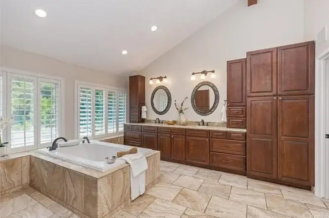 Bathroom with large tub, wooden cabinets, dual round mirrors, and windows