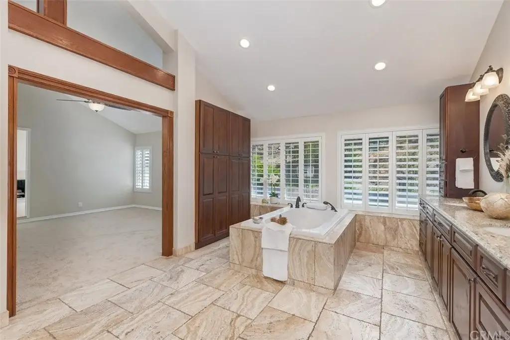 Bathroom with large tub, dual sinks, dark wooden cabinets, and beige tile floor