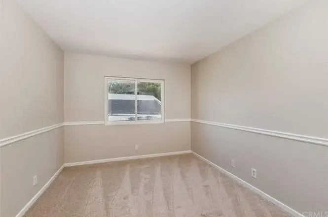 Room with light beige walls, carpet, window, and white trim