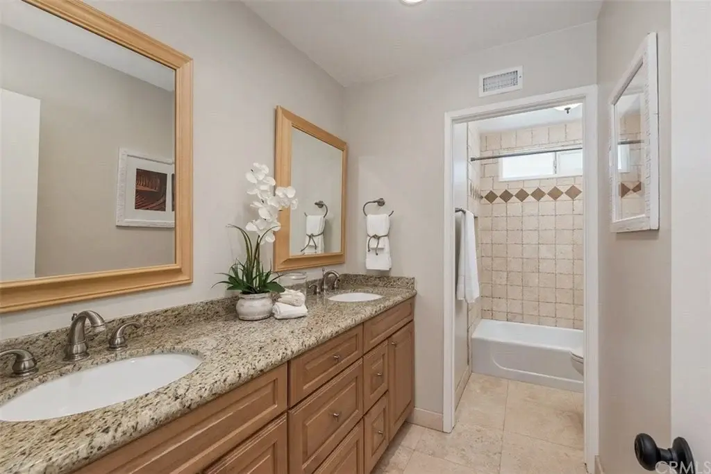 Bathroom with two sinks, wooden cabinets, granite countertops, mirrors, and bathtub
