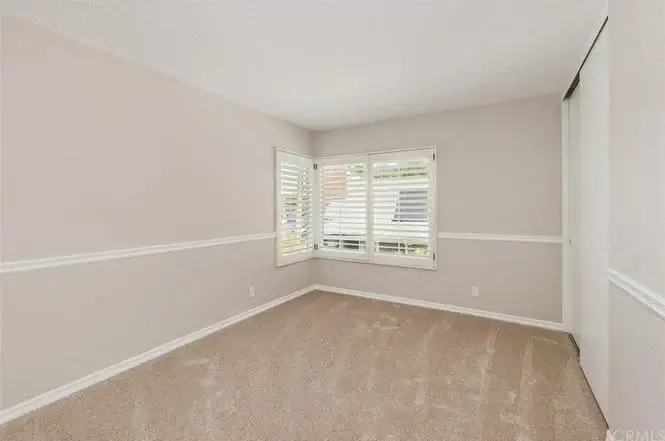 Room with beige walls, carpet, white shutters, and chair rail
