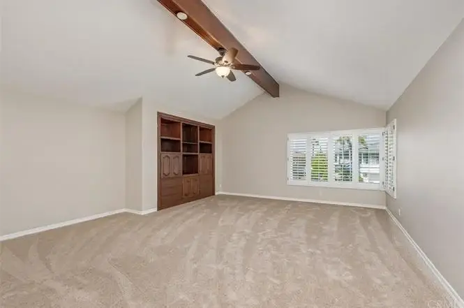 Room with beige carpet, ceiling fan, vaulted ceilings, wooden cabinet, and window