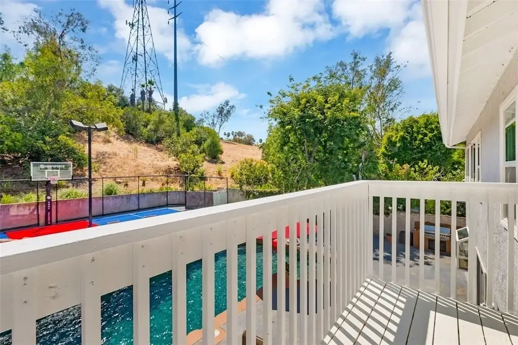 Balcony view with swimming pool, basketball court, trees, and hillside