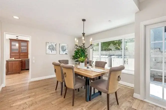Dining room with wooden table, six chairs, chandelier, and plant centerpiece
