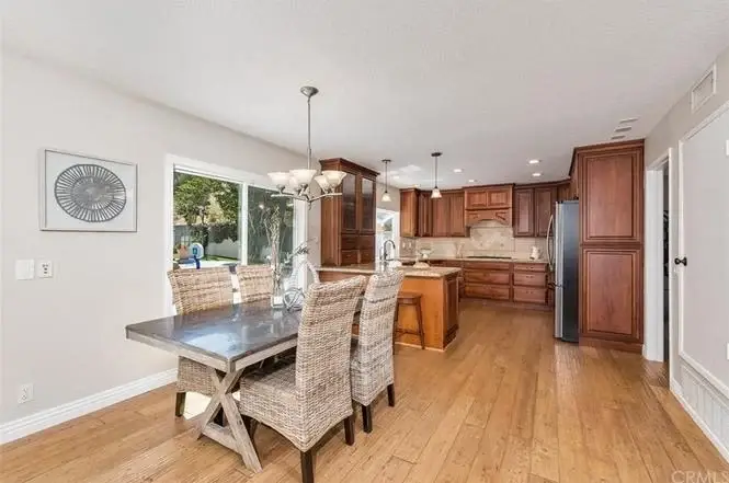 Kitchen with wooden cabinets, large island, dining table with woven chairs, and big windows.