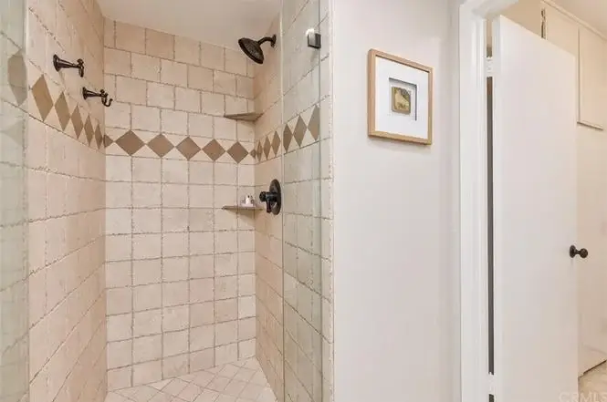 Shower with tiled walls, rainfall showerhead, corner shelf, and decorative tiles.