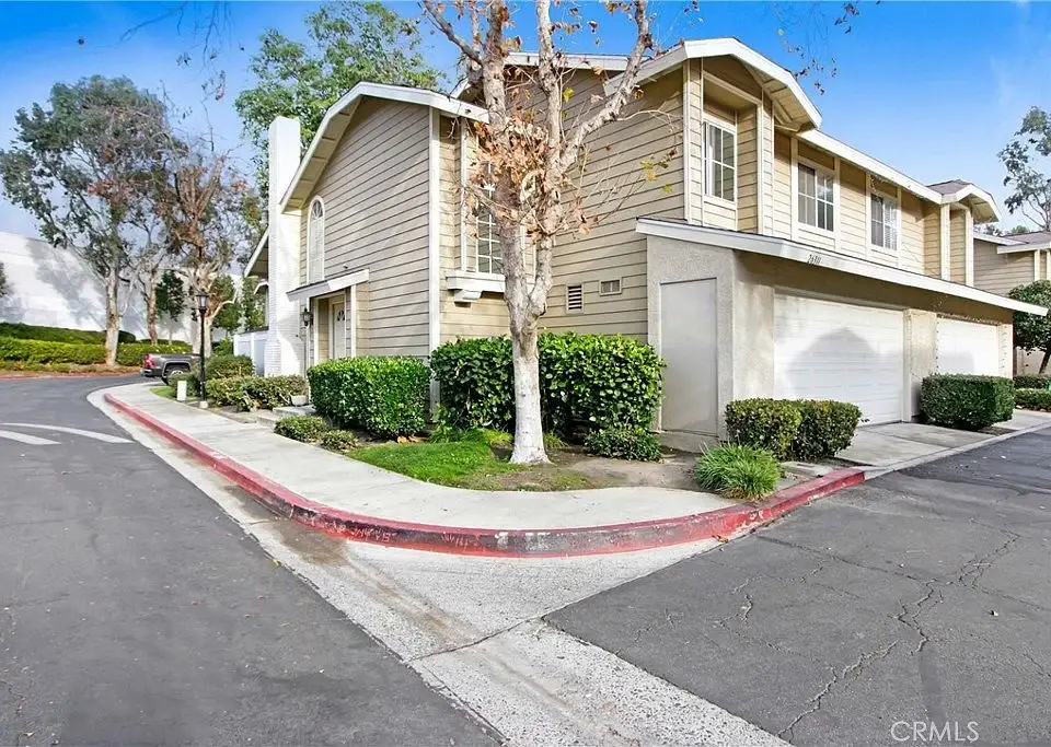 Two-story residential building, California real estate, with driveway, surrounded by bushes and trees