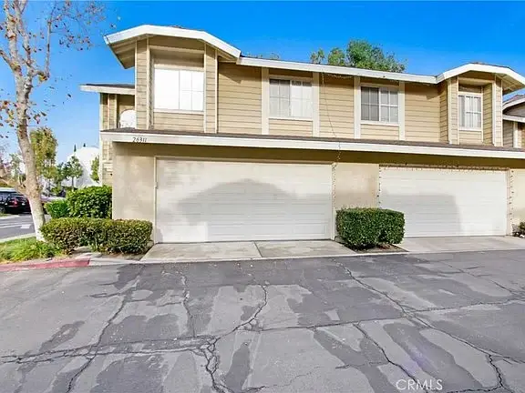 Two-story house with light-colored facade, garage doors, and front landscaping
