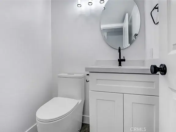 Bathroom with white toilet, sink with countertop, circular mirror, and stylish lighting