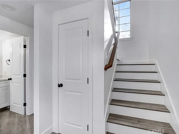 Hallway with white walls, sloped ceiling, wooden floor, arched windows, and white cabinets