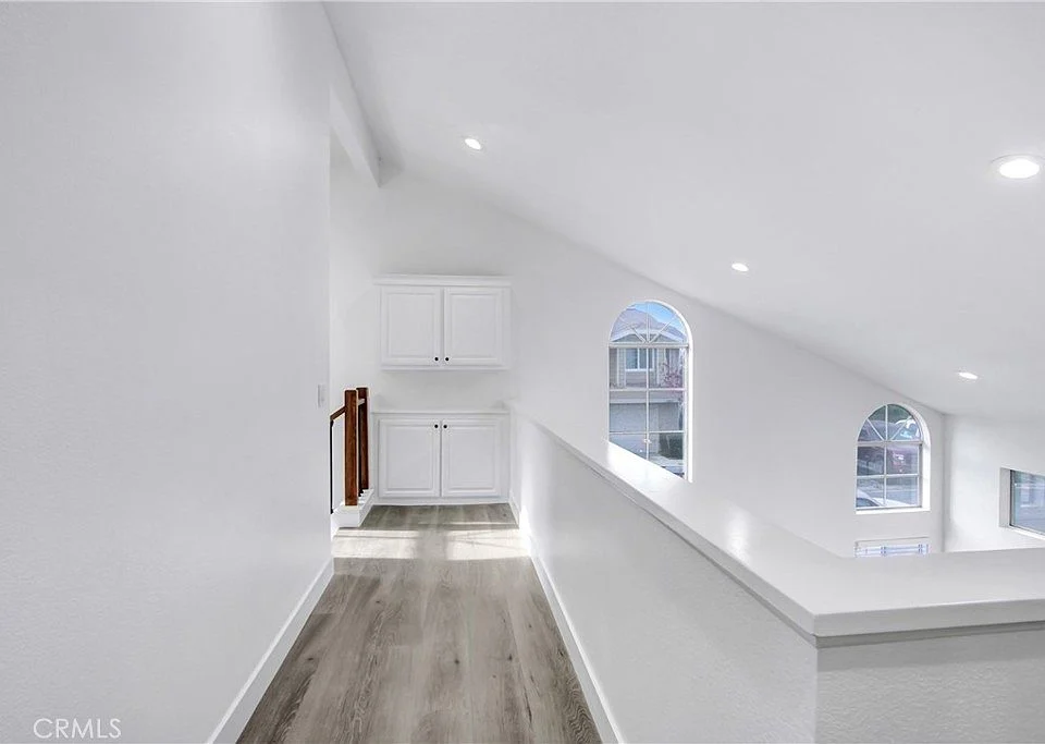 Hallway with staircase, white walls, light wood floors, and door on left side