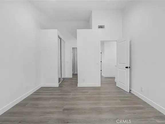 Empty room with light walls, wooden floor, closet on left, and doorway to another spac