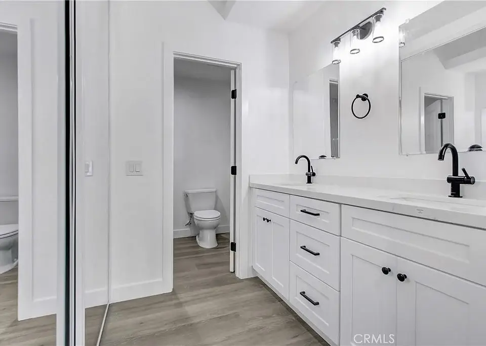 Bathroom with double sink vanity, black faucets, large mirrors, tile floor, and separate toilet area
