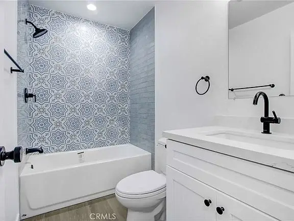 Bathroom with tub, patterned wall tiles, white cabinets, and modern mirror
