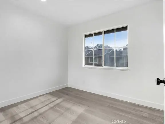 Empty room with white walls, light wood floor, and window on right wall