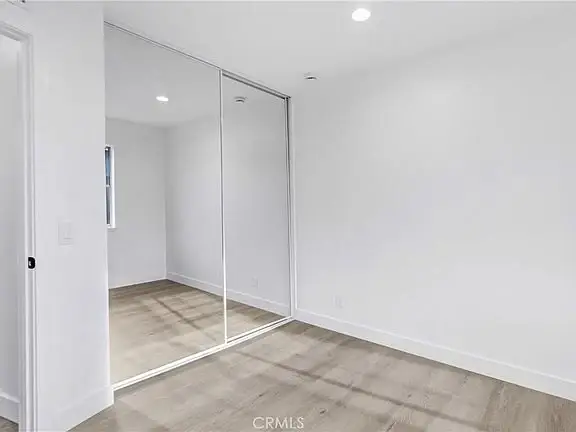 Empty room with white walls, wooden floor, mirrored closet doors, and small window