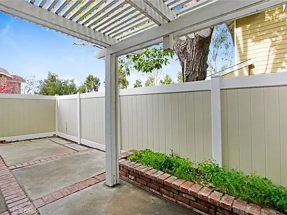 Covered patio with wooden frame, beige fence, red brick garden bed, and green plants