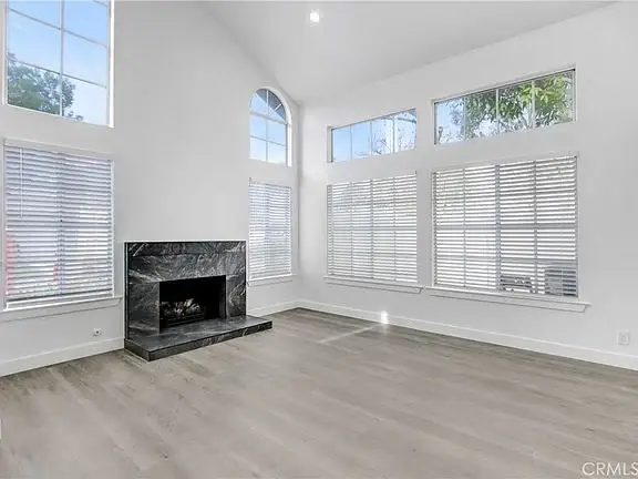 Living room with large windows, tall ceiling, modern fireplace, and light hardwood floor