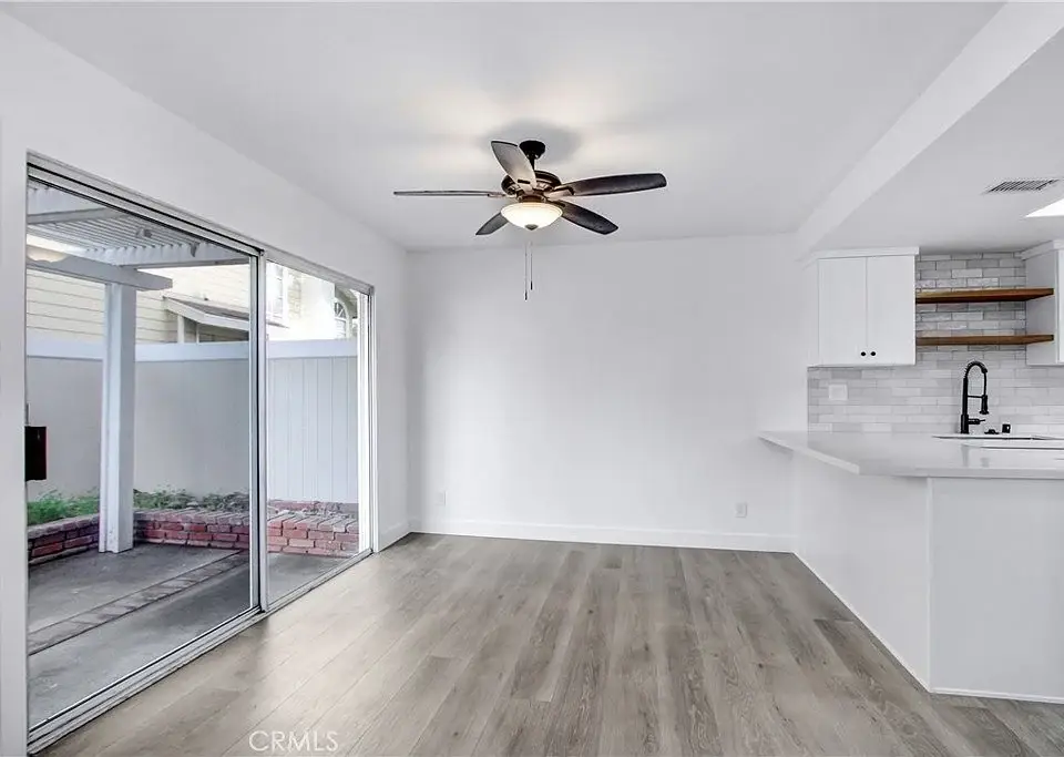 Living space with laminate floor, ceiling fan, sliding doors to outdoor area, and kitchen with light cabinets and sink