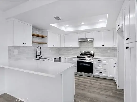Kitchen with white cabinets, black gas stove, stainless steel appliances, island with sink, and wood accents
