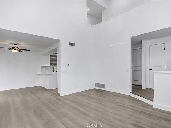Spacious room with light walls and floor, ceiling fan, and open layout to kitchen