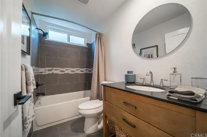 Bathroom with bathtub, shower, gray tile, and wooden vanity with dark countertop