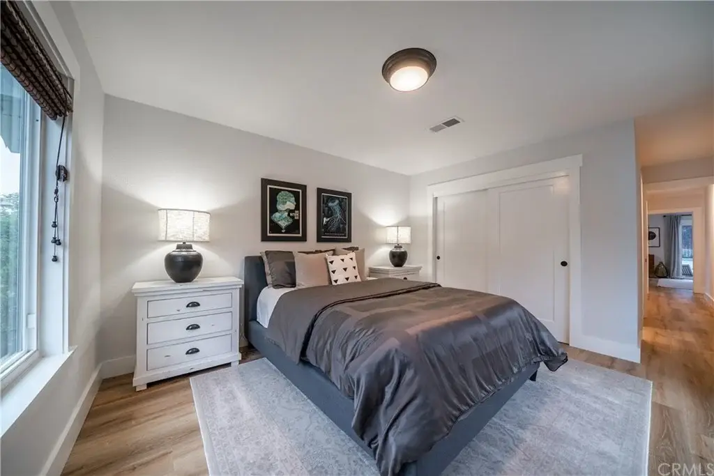 Bedroom with gray bed, two bedside lamps, framed artwork, and light-colored rug