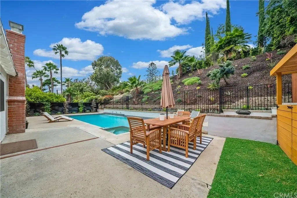 Backyard with swimming pool, dining table under umbrella, and palm trees