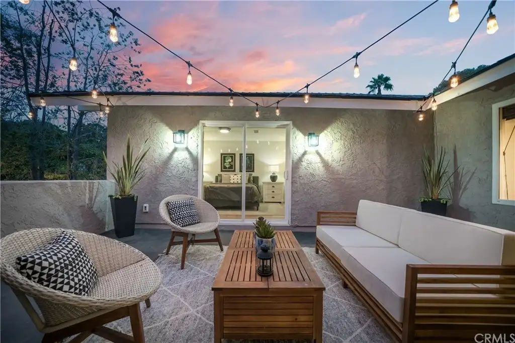 Outdoor patio with wooden coffee table, two wicker chairs, cream sofa, and glass door to interior