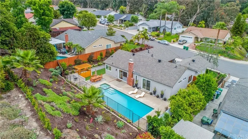 Aerial view of houses with green lawns, trees, backyard with swimming pool, and landscaped gardens