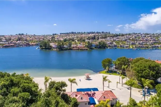 Aerial view of lake with greenery, residential buildings, and sandy beach