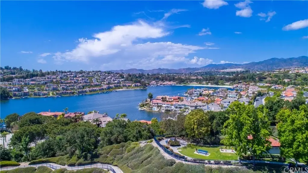 Aerial view of lake with houses, green hills, and boat on water, California real estate