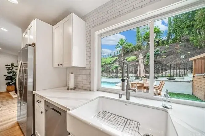 Kitchen with white cabinets, farmhouse sink, windows, and view of yard with pool and outdoor seating