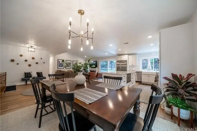 Dining room with wooden table, black chairs, chandelier, windows, plants, and wall art