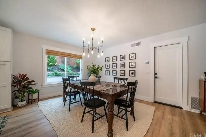 Dining room with wooden table, black chairs, window, plants, and wall art